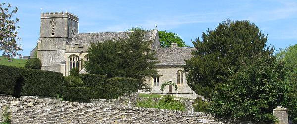 View over a low stone wall to a limestone built church with a tower